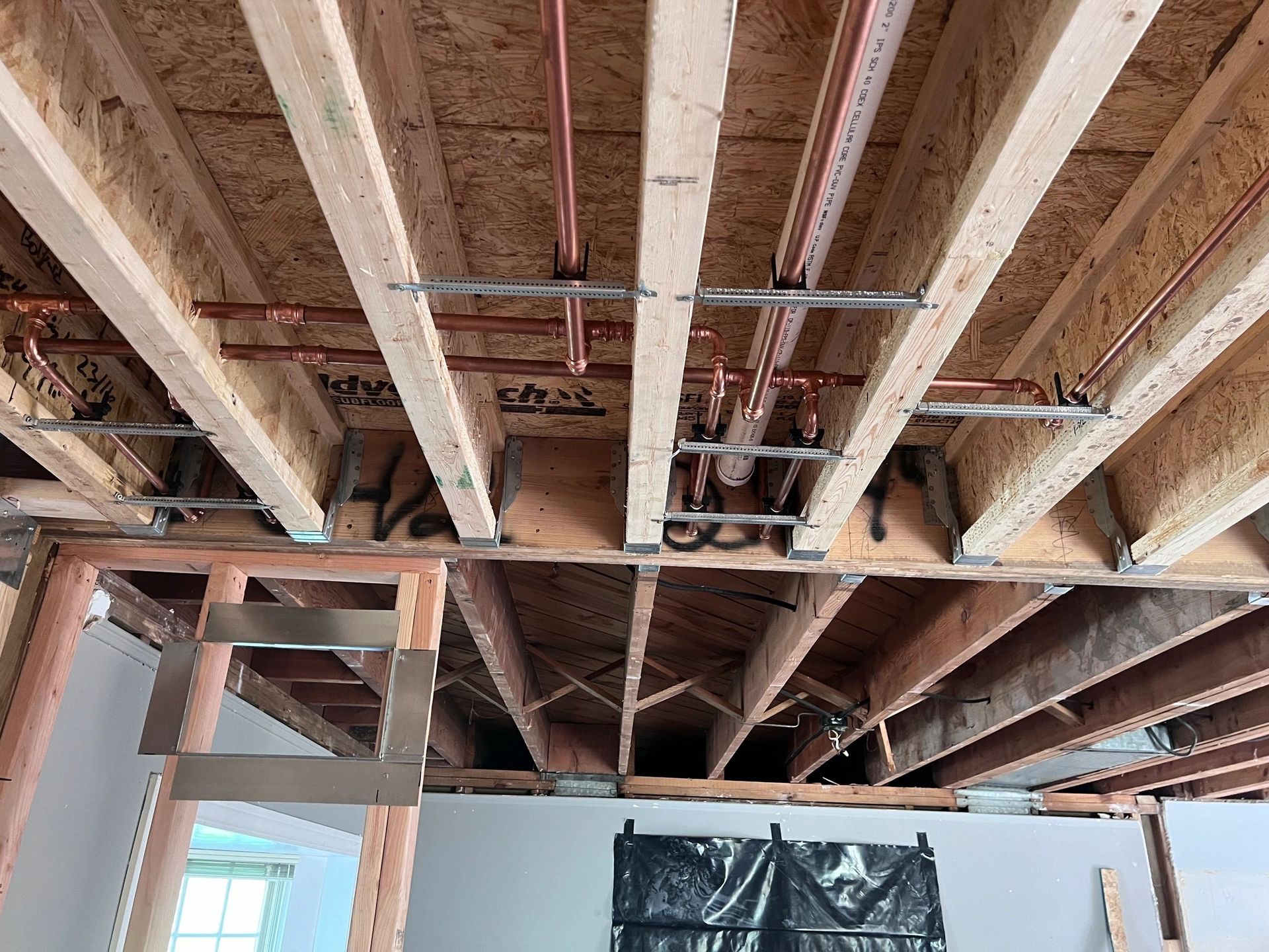 The ceiling of a house under construction with pipes coming out of it.