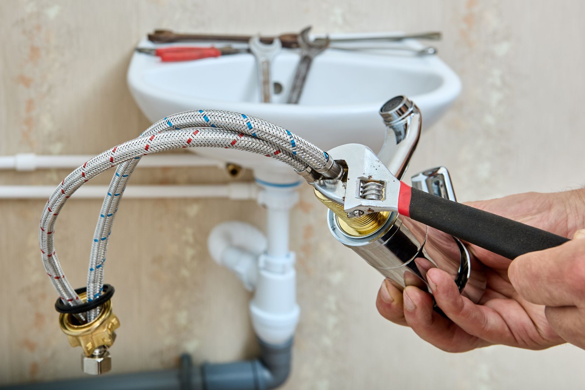 Person using a wrench to connect a flexible hose to a bathroom faucet in front of a white sink.