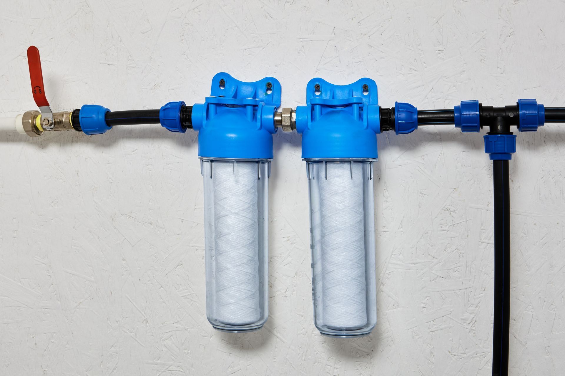 Two blue water filter housings attached to pipes on a white wall.