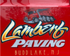 Red sign for Lambert Paving of Budd Lake, NJ, with a cartoon dump truck in the logo.