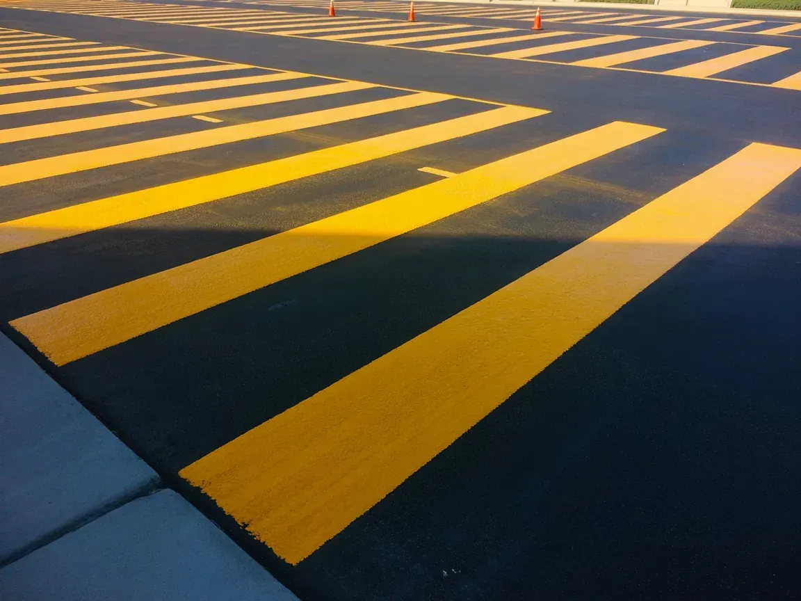 Yellow striped pavement markings on asphalt, likely a crosswalk or caution area.