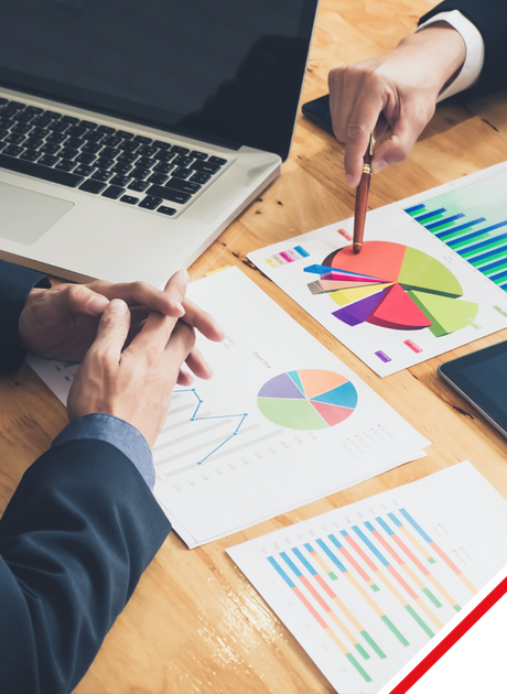 Two business people review charts and graphs at a table with a laptop and phone.
