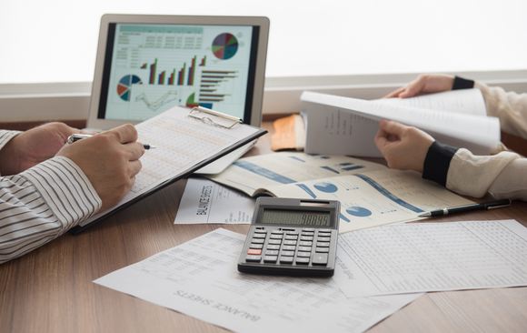 People reviewing financial documents with a laptop displaying graphs and a calculator on a desk.