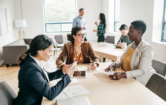 Business meeting: diverse group around a table, looking at documents and a tablet.