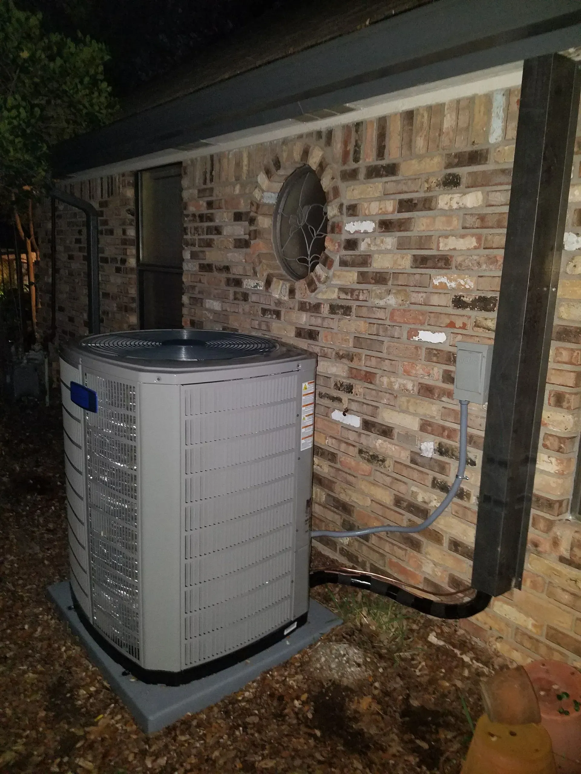 An air conditioner is sitting on the side of a brick house.