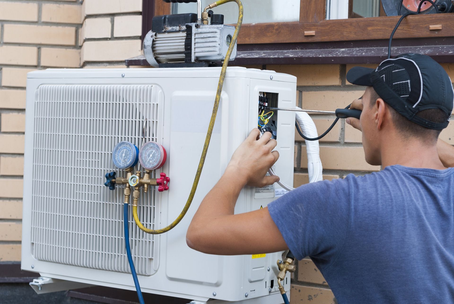 HVAC contractor installs an air conditioning unit outside a home, next to a brick wall and a window.