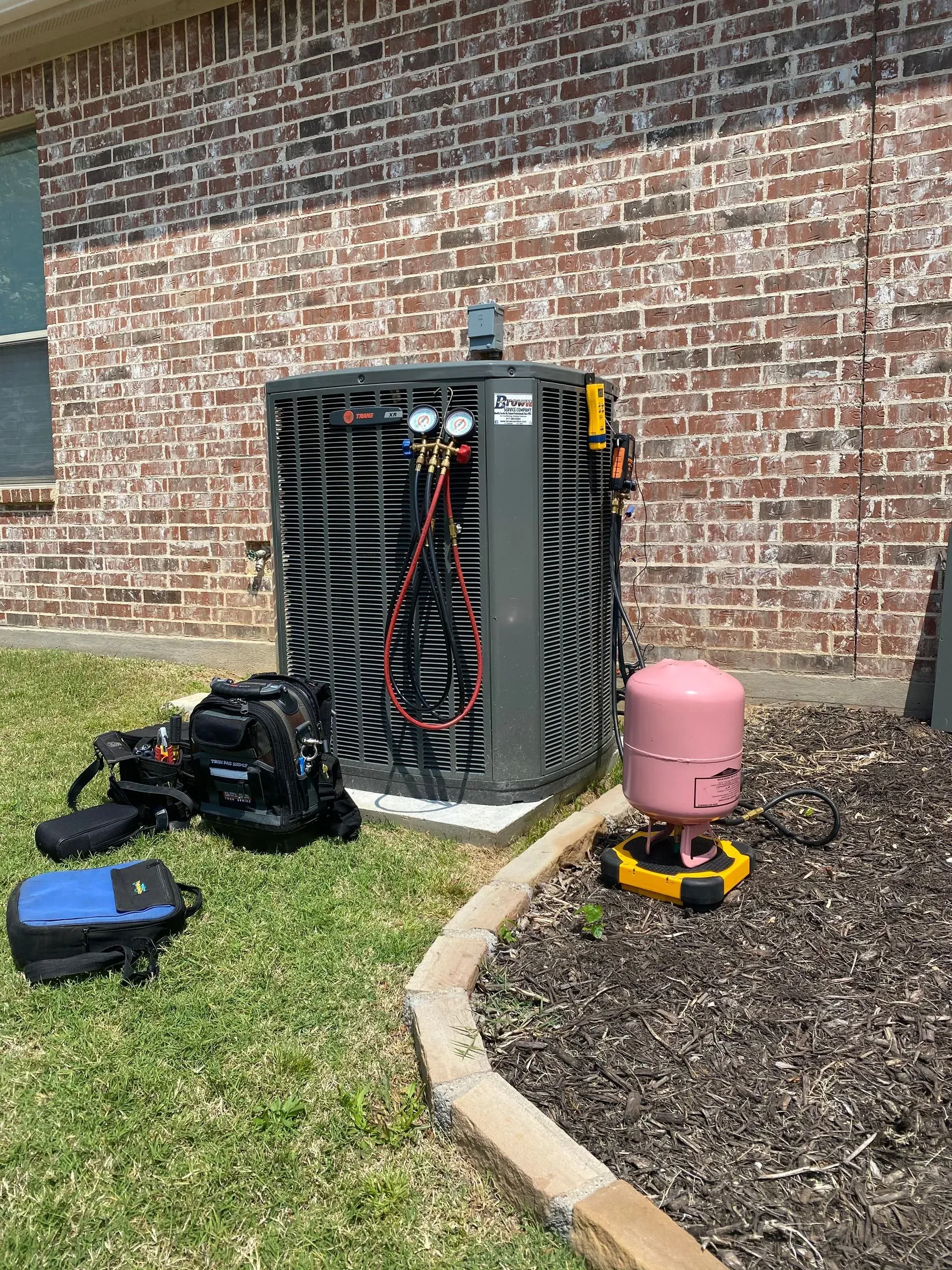 An air conditioner is being repaired in the backyard of a brick house.