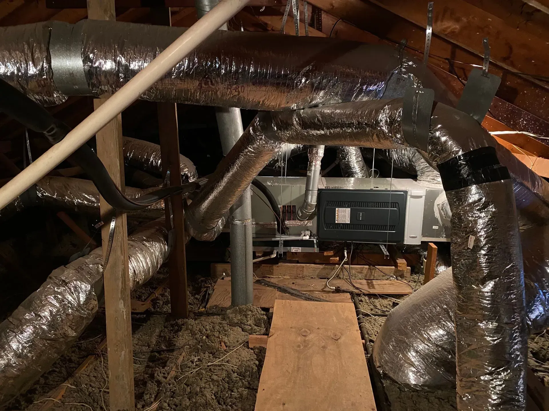 A bunch of ducts are hanging from the ceiling of an attic.
