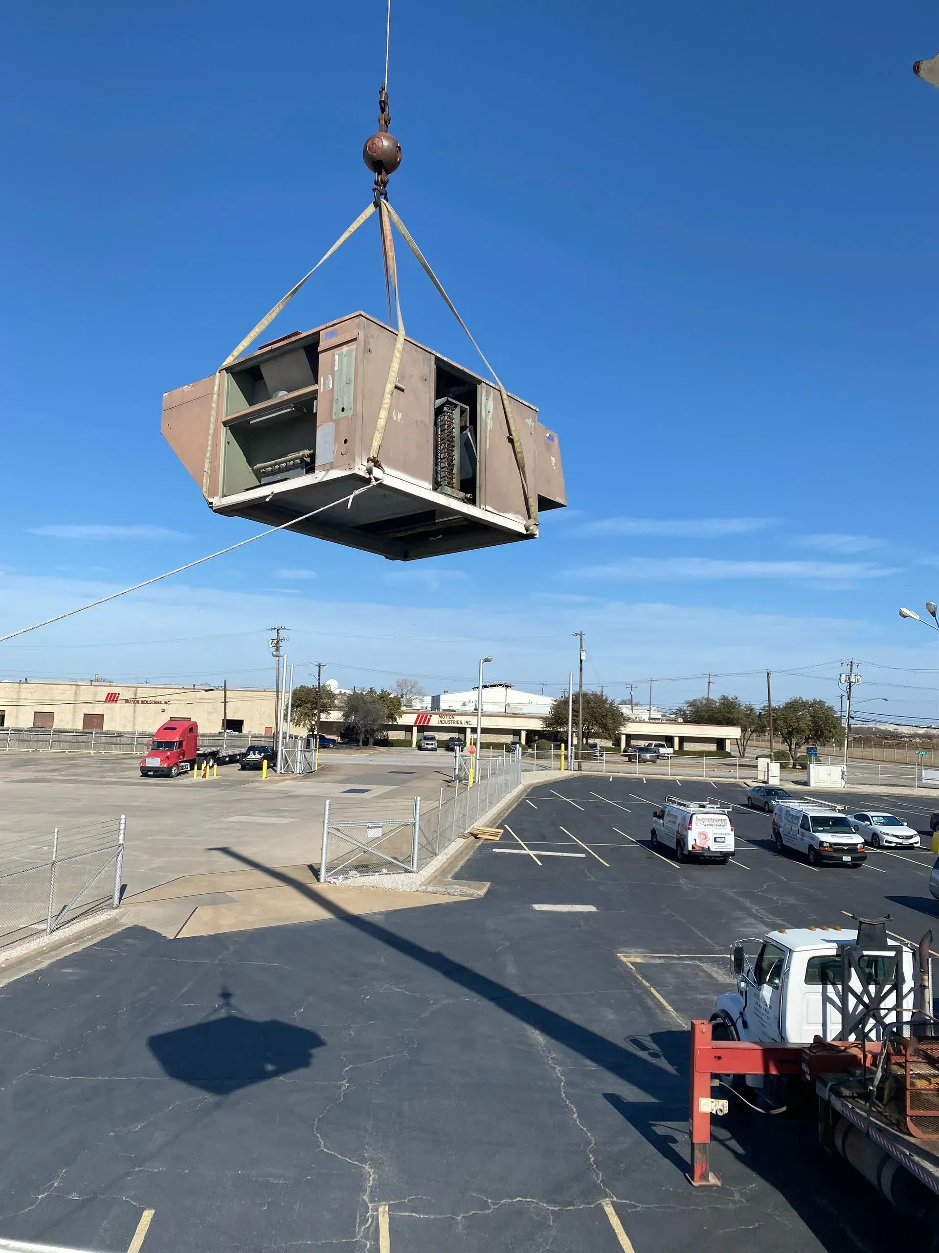 A large piece of equipment is being lifted by a crane in a parking lot