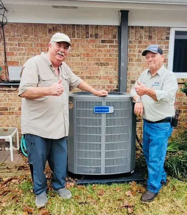 Two men are standing next to an air conditioner and giving a thumbs up.