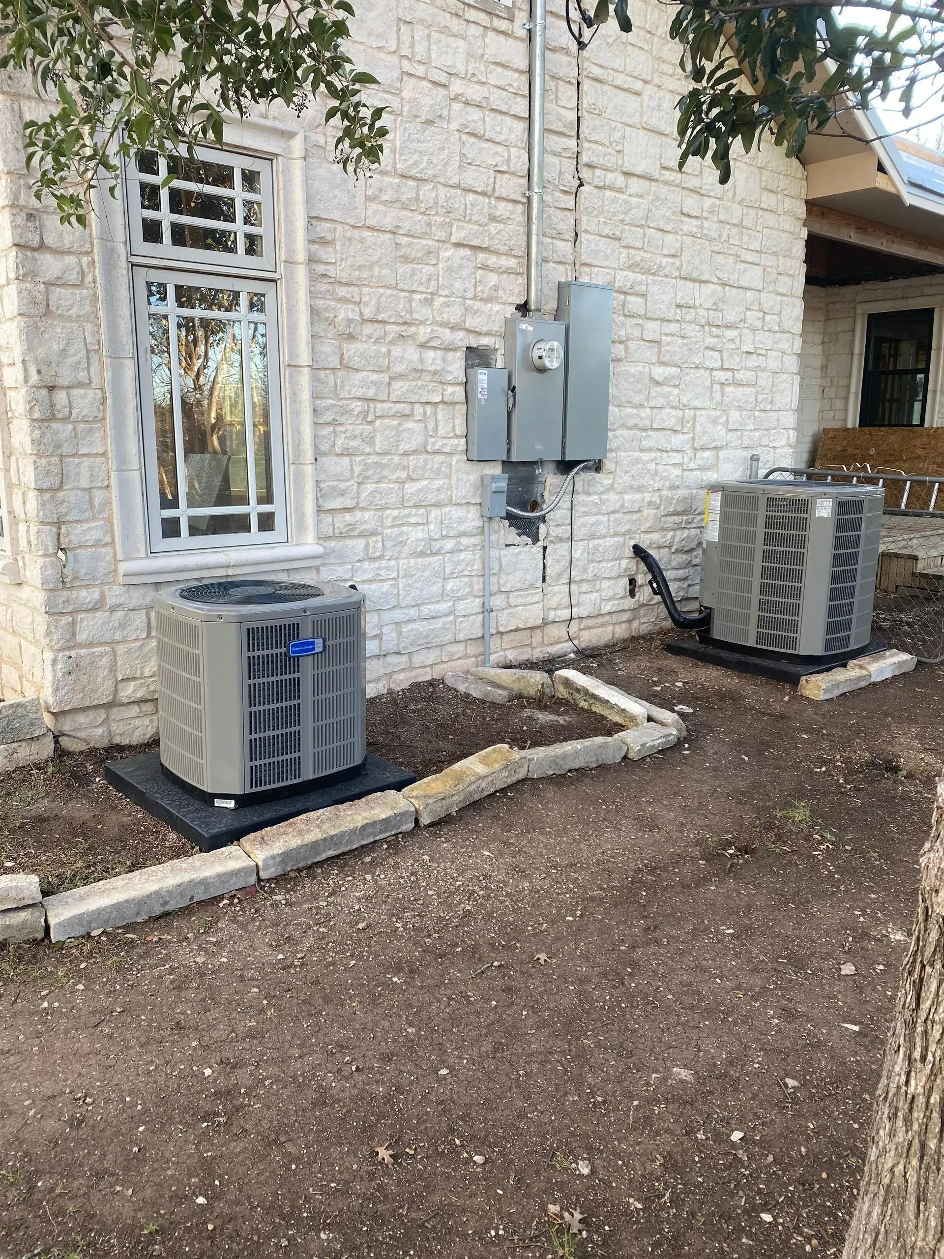 Two air conditioners are sitting in front of a brick building.