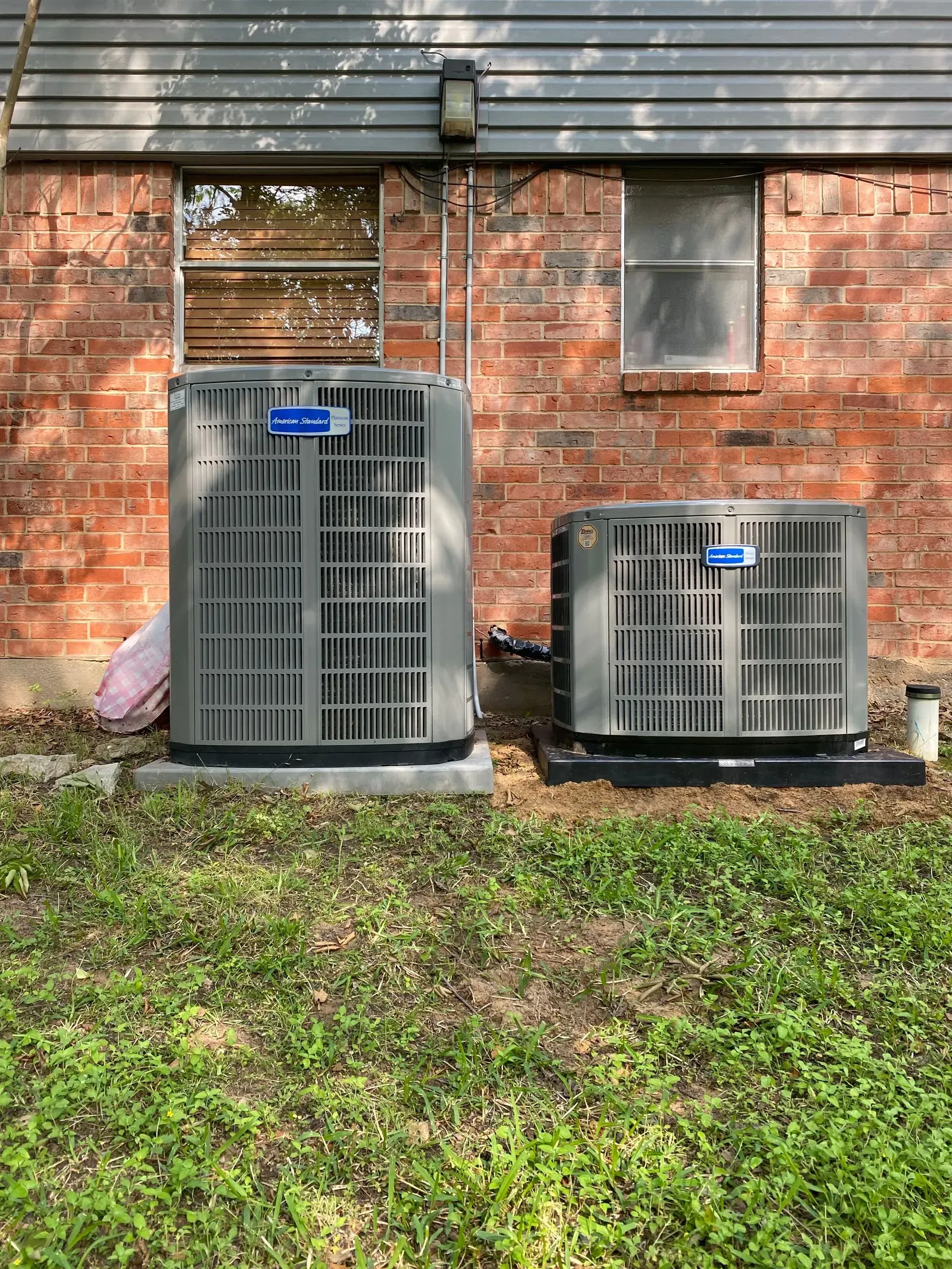 Two air conditioners are sitting on the side of a brick building.