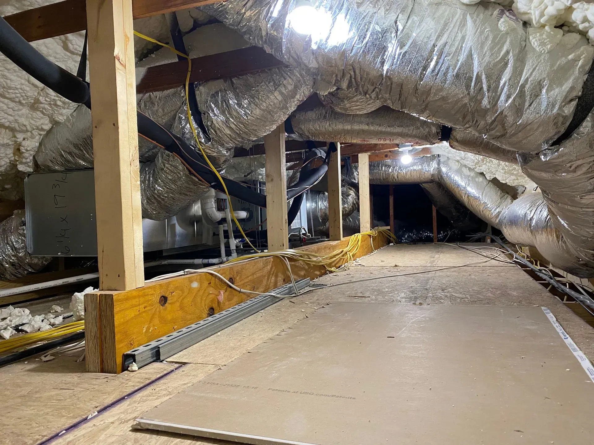 An attic with a lot of pipes and wires coming out of it.