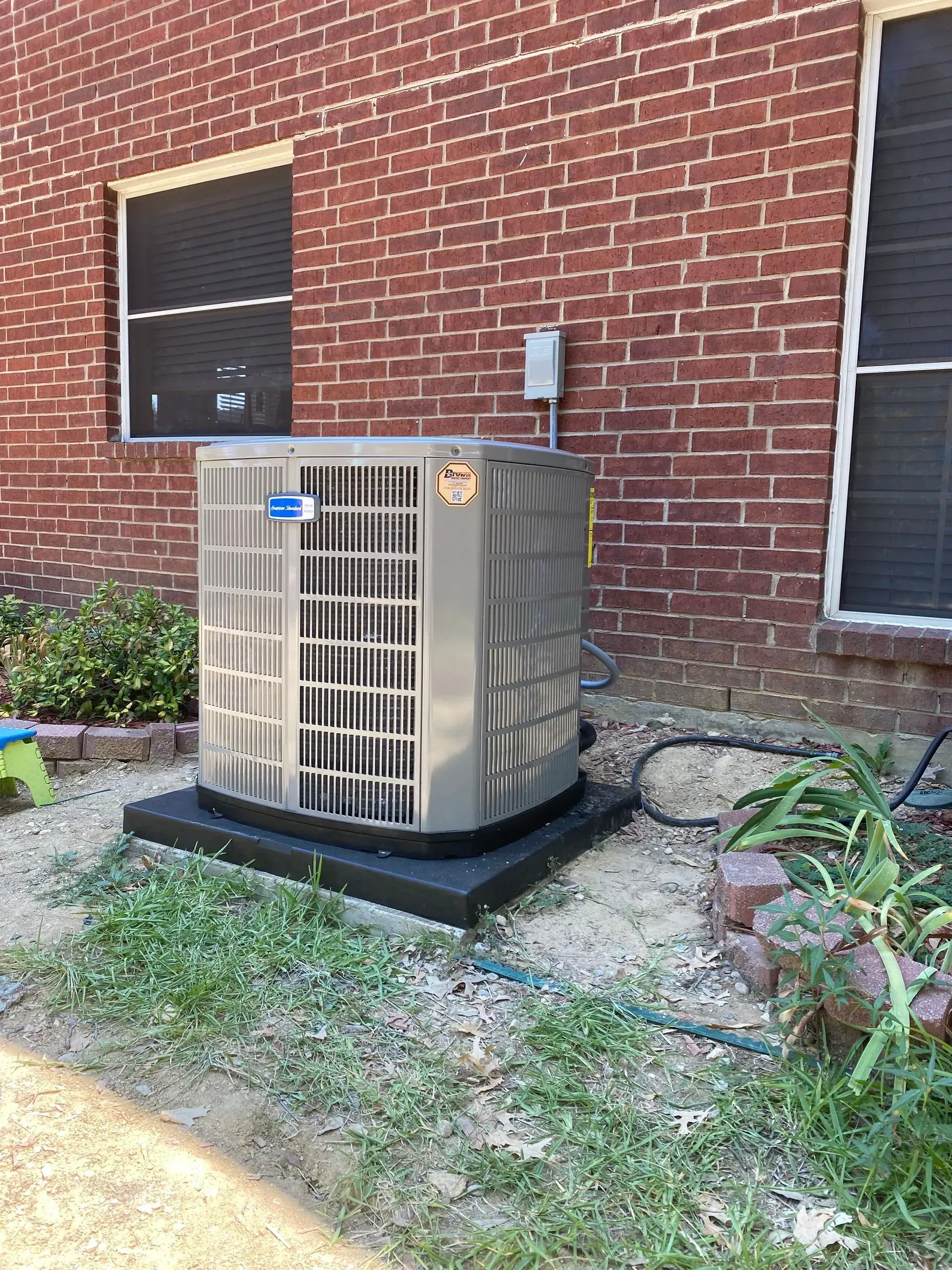 An air conditioner is sitting on the side of a brick building.