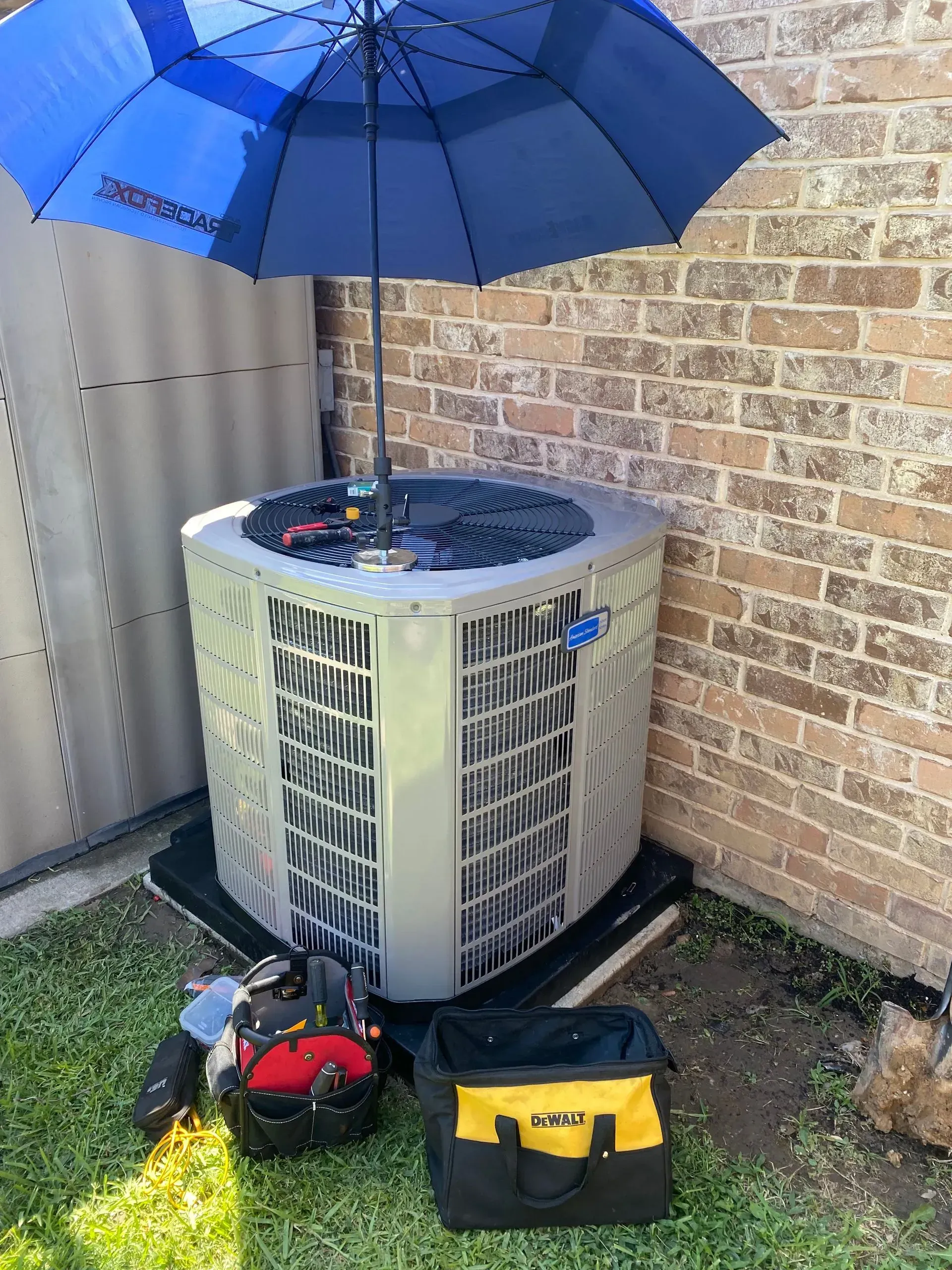 An air conditioner is sitting under an umbrella next to a brick wall.