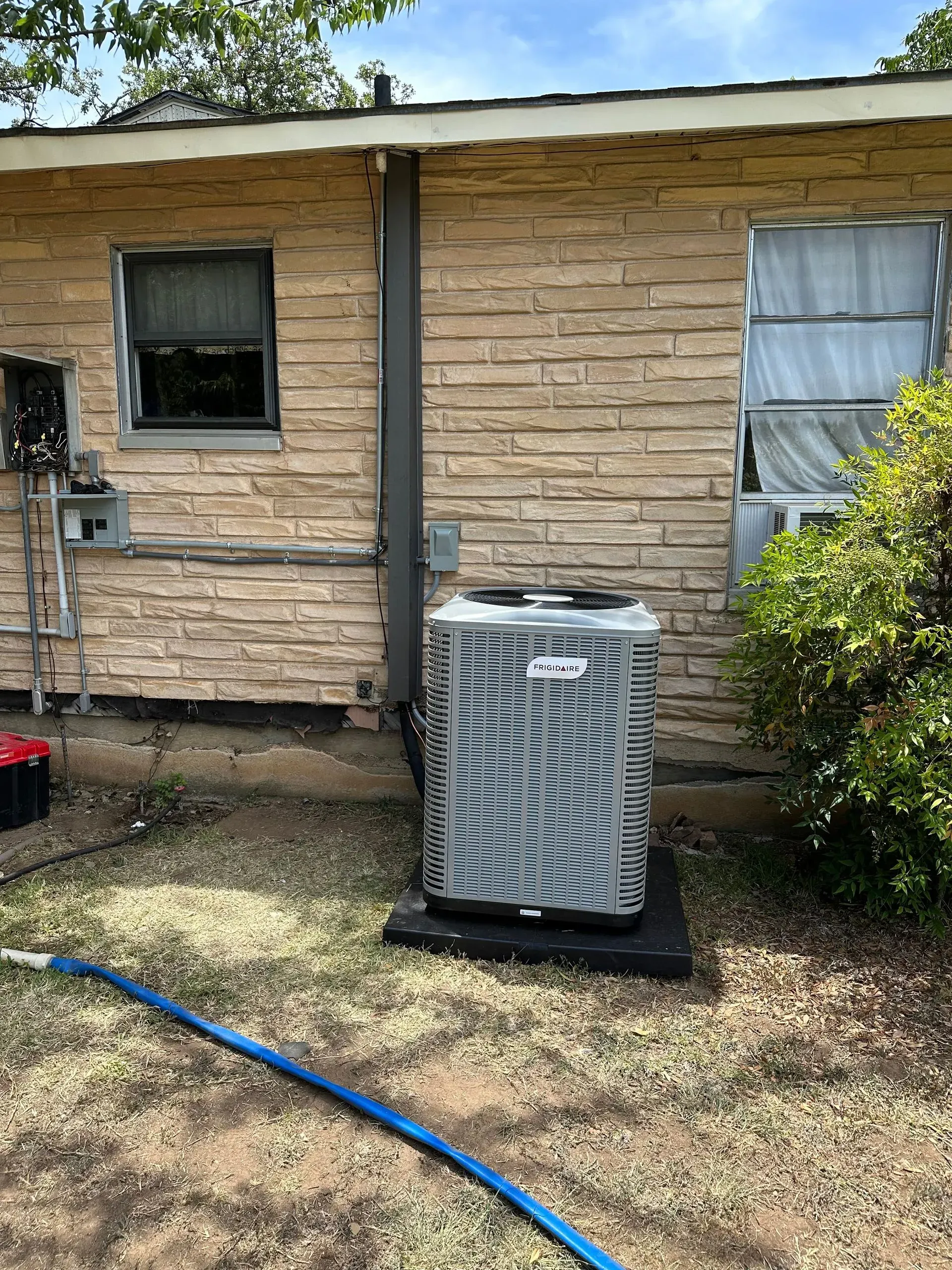 An air conditioner is sitting on the side of a brick house.
