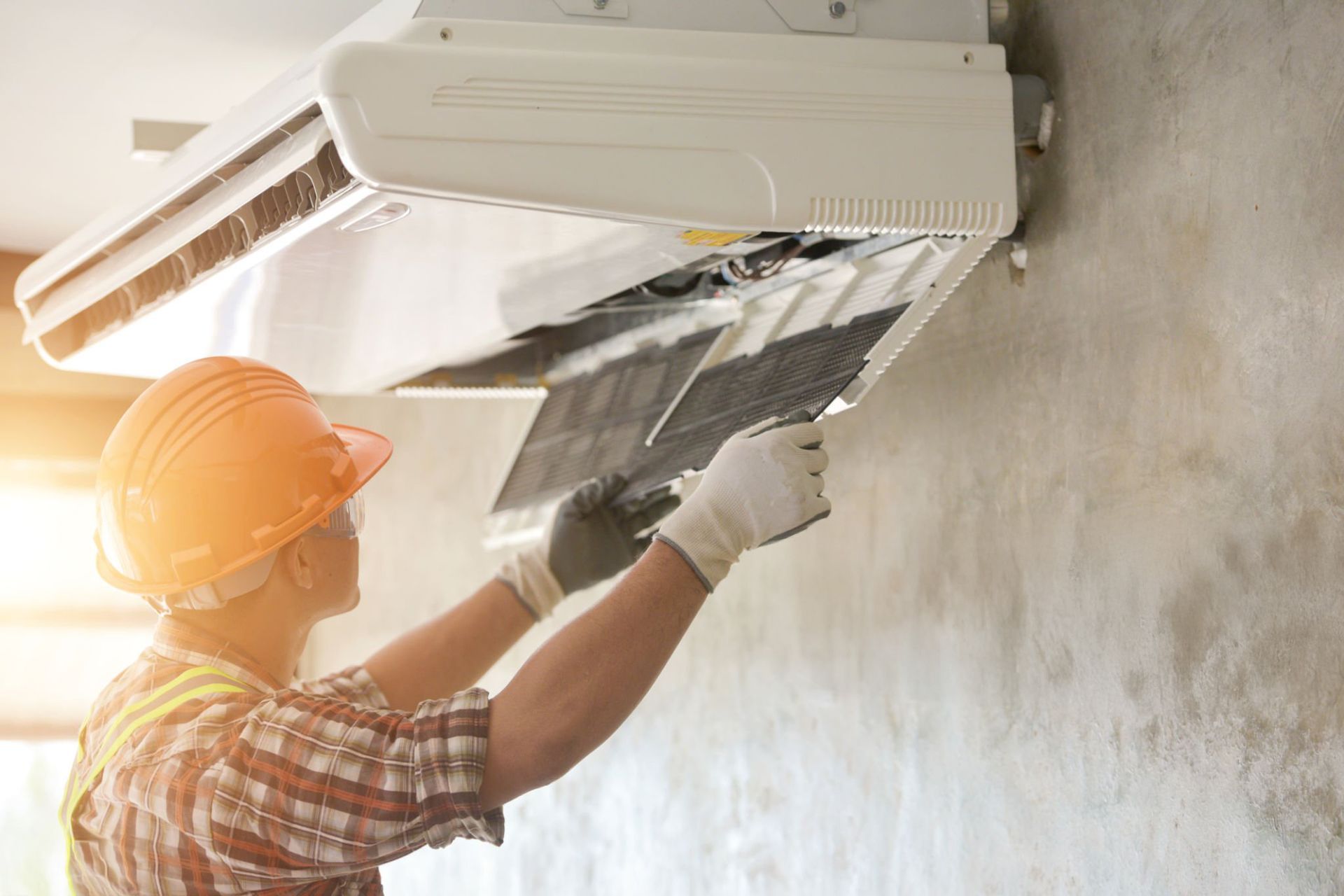 Worker in hard hat repairing wall-mounted air conditioner. Worker in hard hat repairing wall-mounted air conditioner.