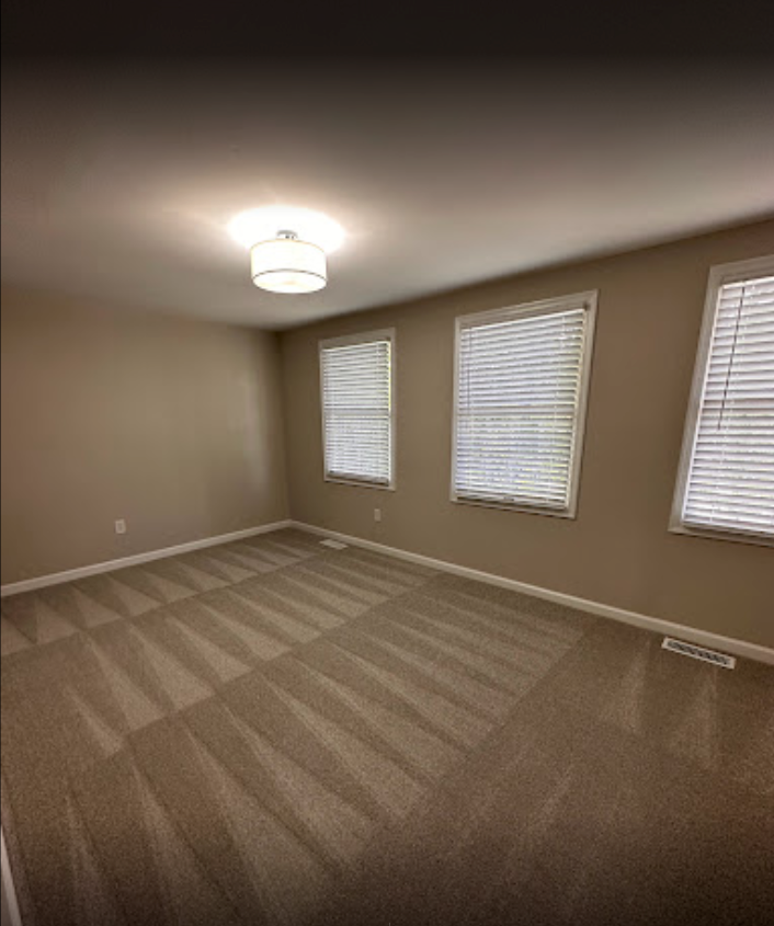 an empty bedroom with a carpeted floor and three windows .