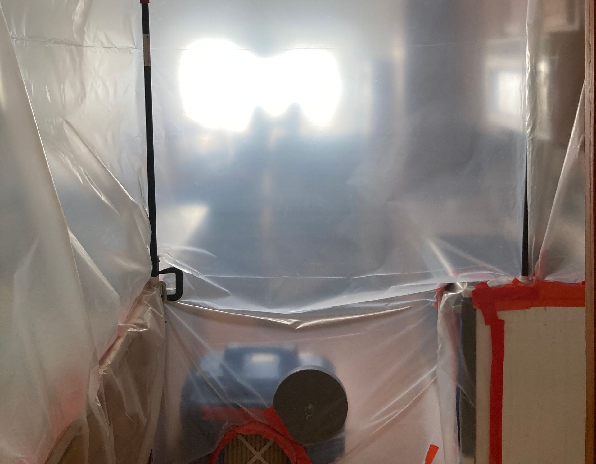 A room is covered in plastic and has a fan in it.