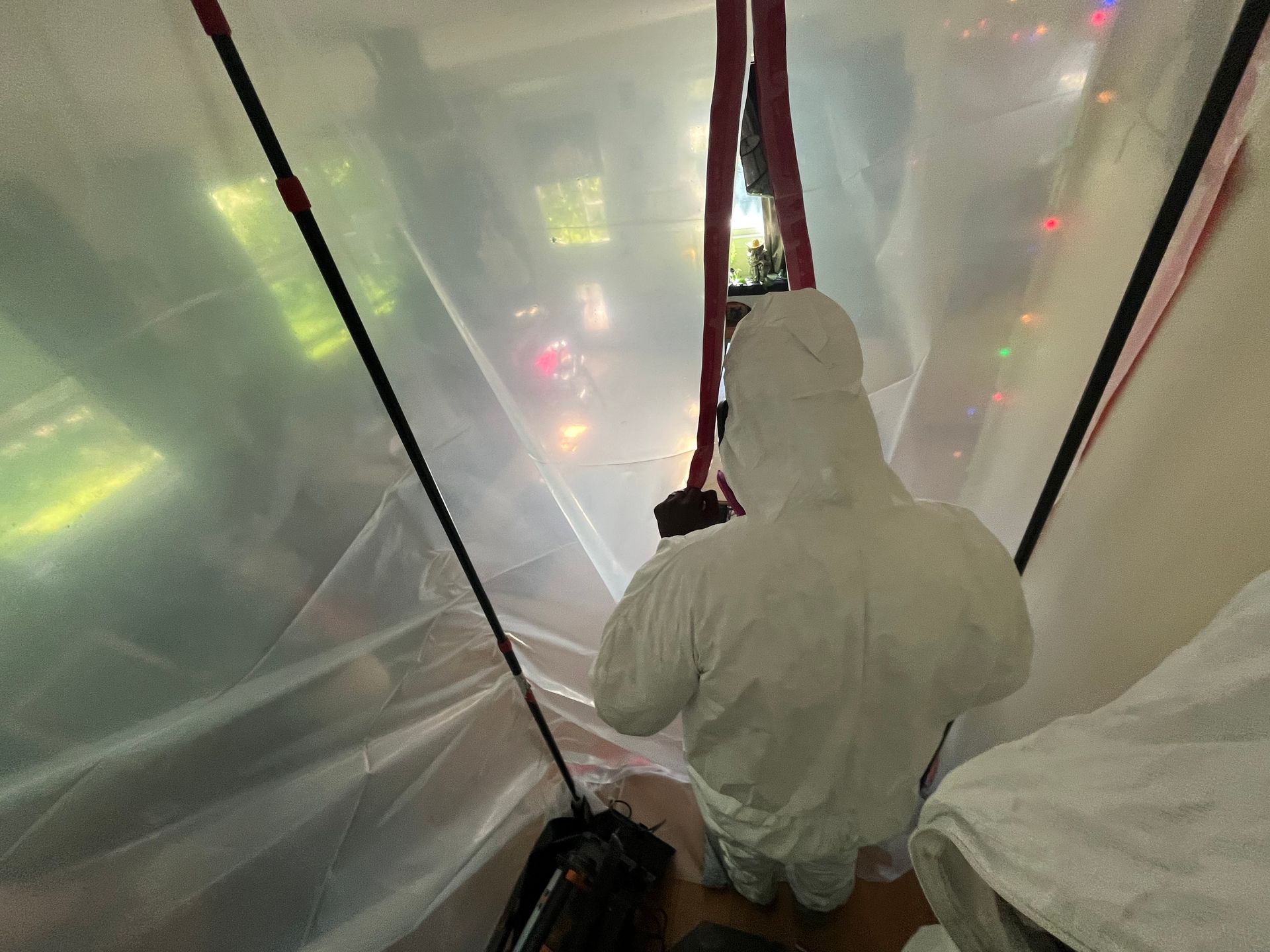 A man in a protective suit is standing in a room covered in plastic.
