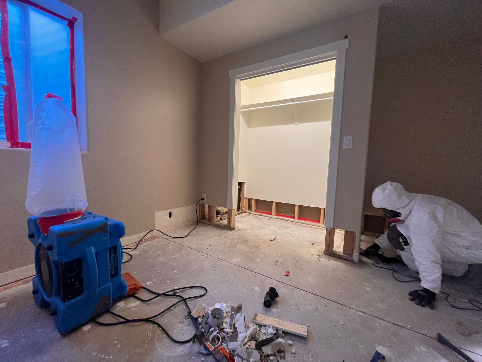 A man in a protective suit is working on a closet in a room.