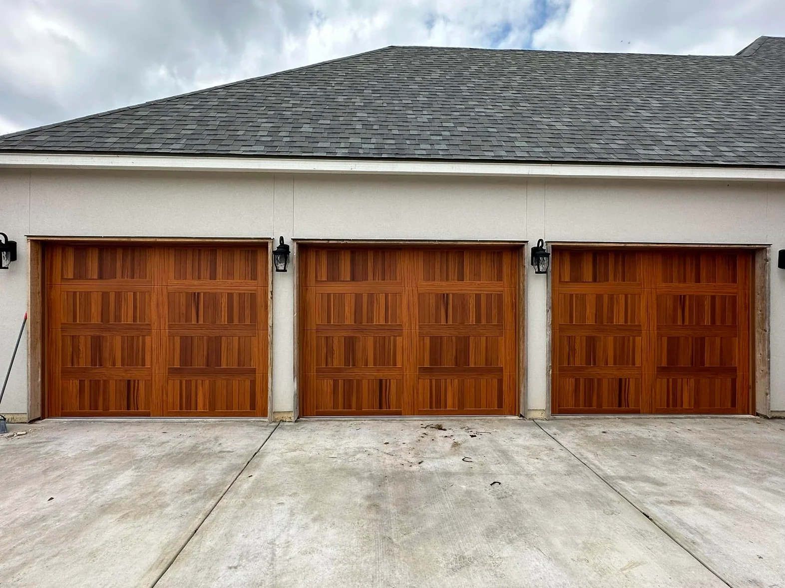 Three wooden garage doors are lined up in front of a house.