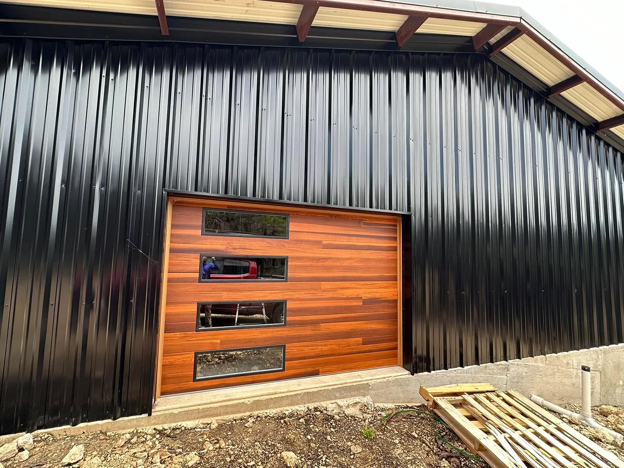 A black building with a wooden garage door and windows.