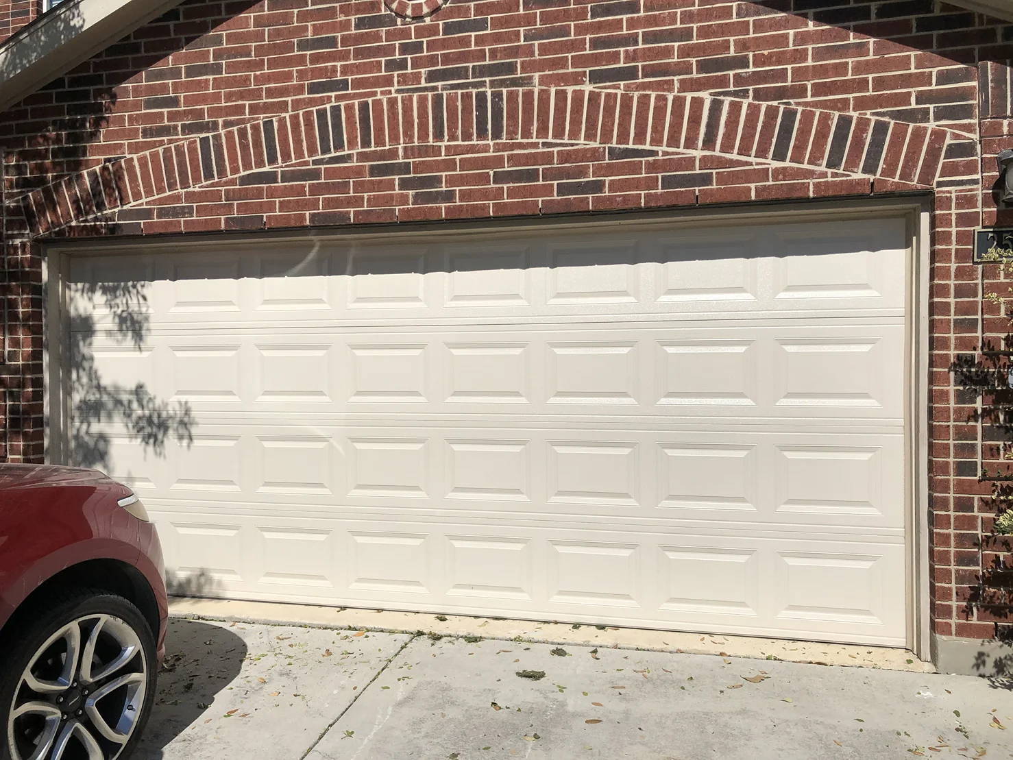 A red car is parked in front of a white garage door.