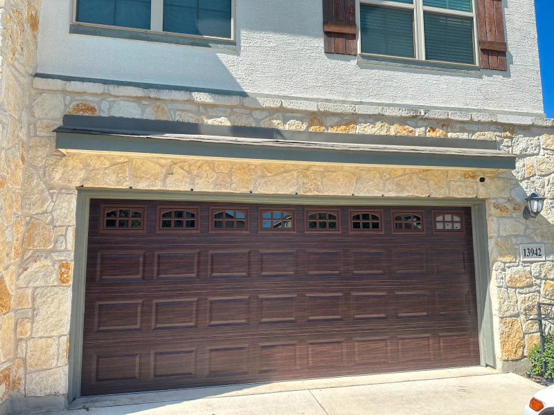 A brown garage door is sitting in front of a stone building.