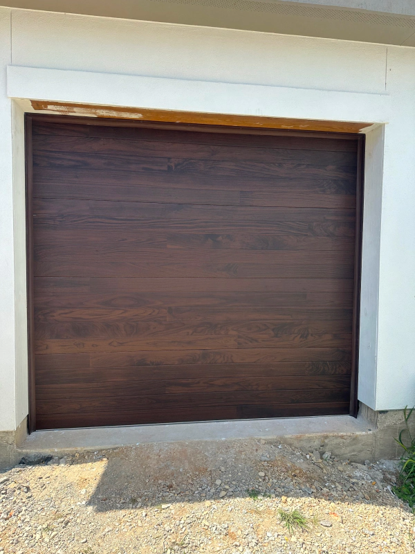 A brown garage door is sitting in front of a white building.