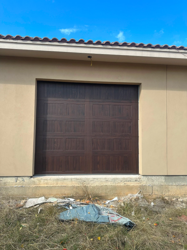 A brown garage door is sitting in front of a house under construction.