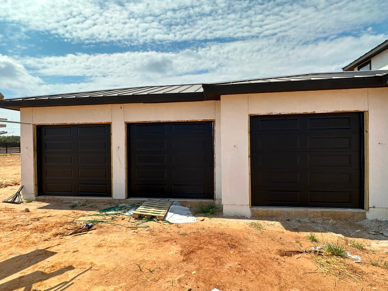 A house under construction with three black garage doors.