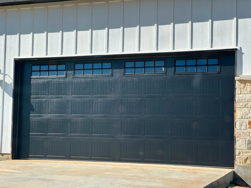 A black garage door is sitting in front of a white building.