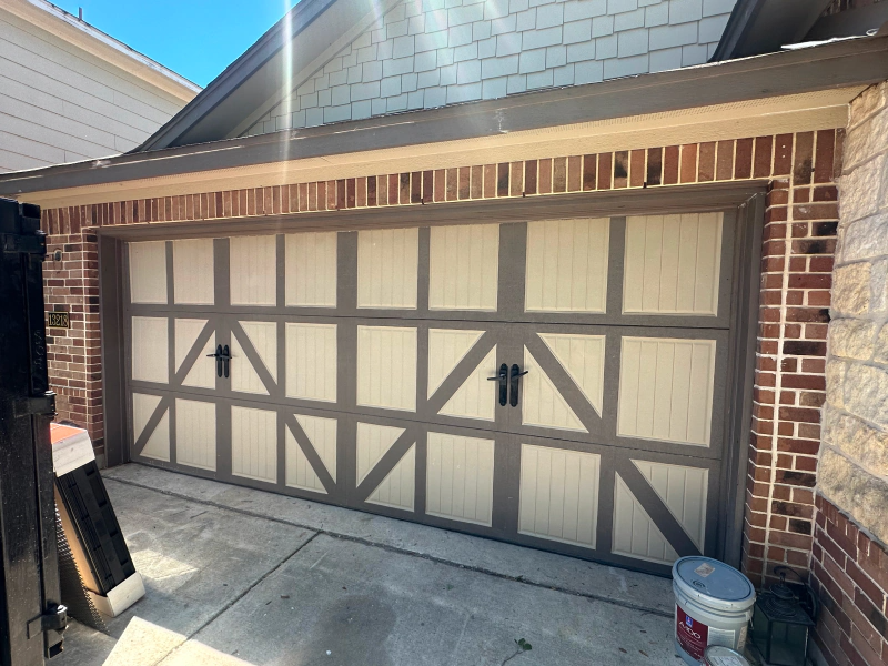 A garage door with a brick wall and a bucket of paint in front of it.