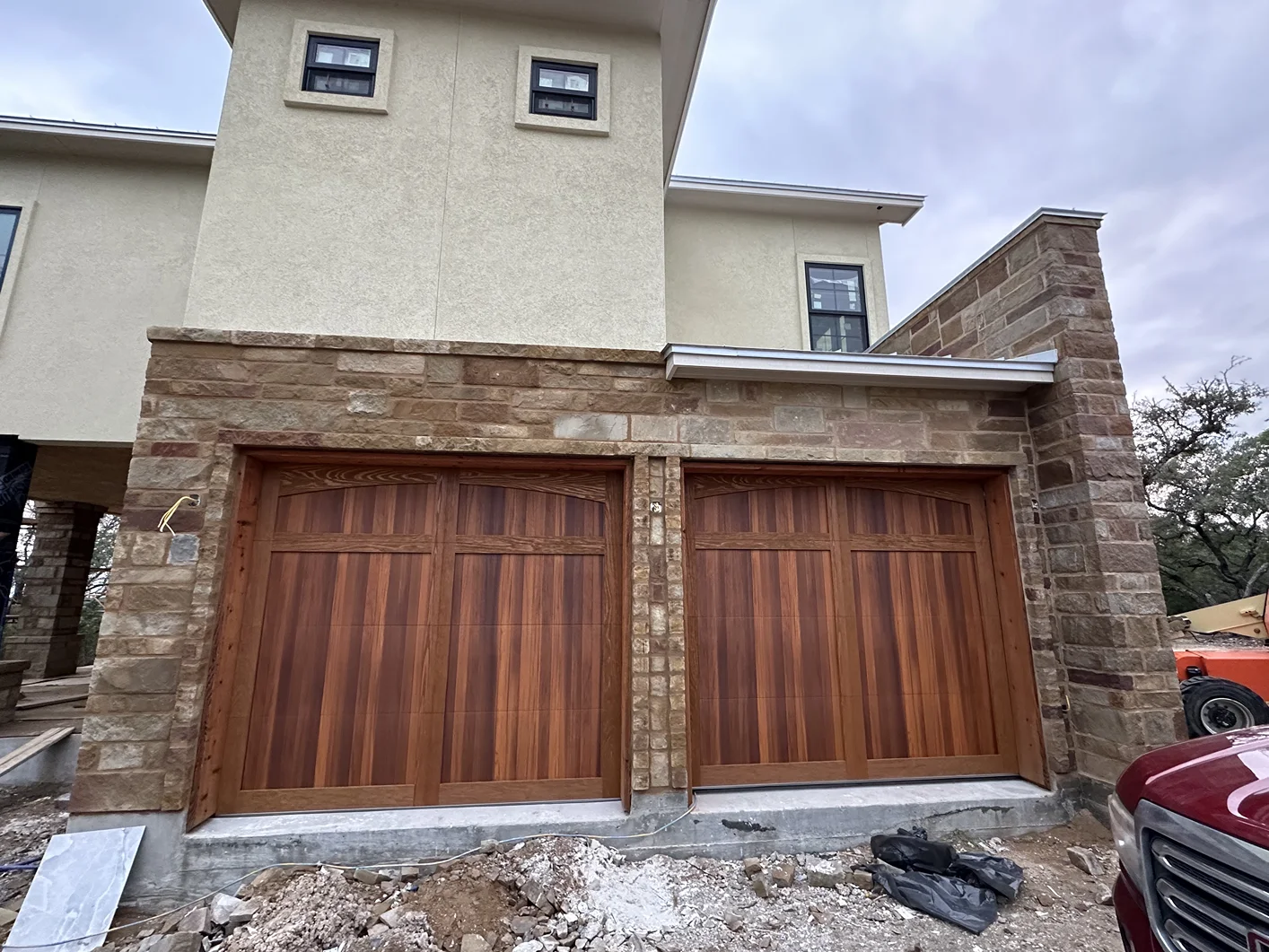 A house with two wooden garage doors and a red truck parked in front of it.