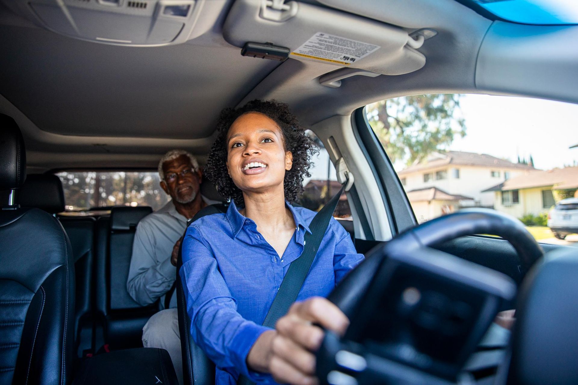 Woman driving a car with a passenger in the back seat, smiling on a sunny street