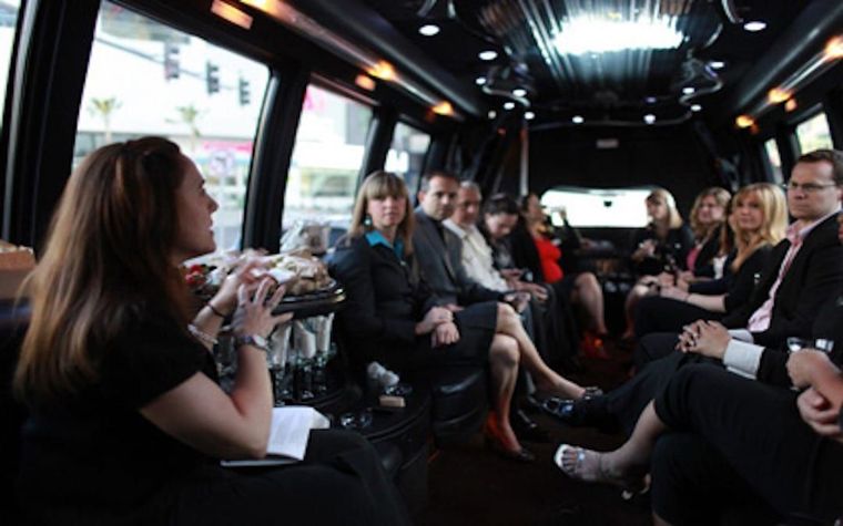 People seated in a van at an indoor meeting, talking and listening in a dim, modern setting