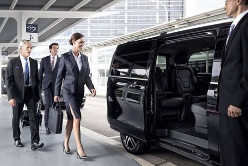 Business professionals arriving beside a black van at a modern building entrance