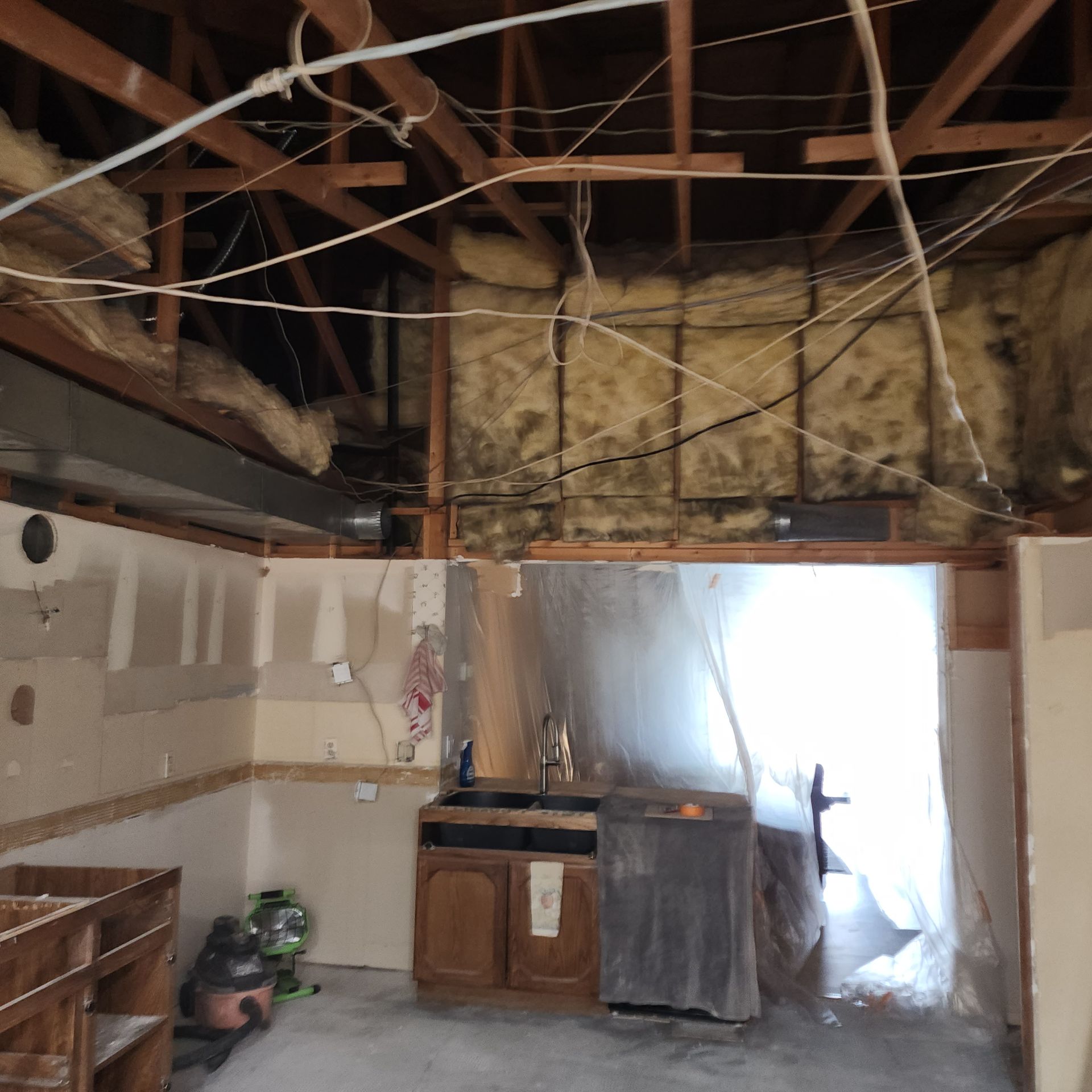 Interior renovation with exposed ceiling and insulation. Kitchen cabinets, sink, and appliances are visible.