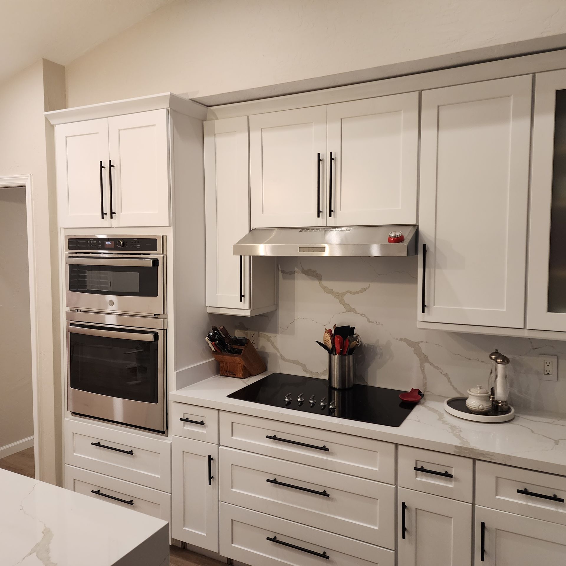 White kitchen with built-in oven, stove, cabinets, and marble backsplash.