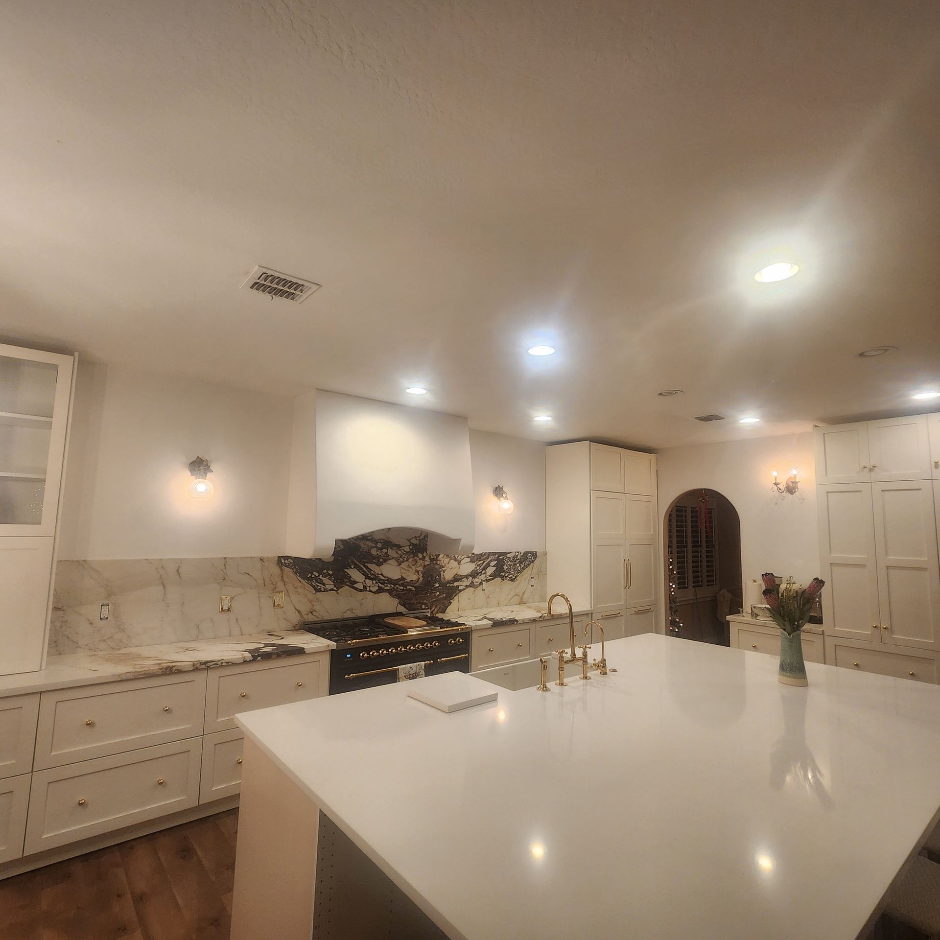 Kitchen with white cabinets, island, and countertops; a stove with a decorative hood and a dark arched doorway.