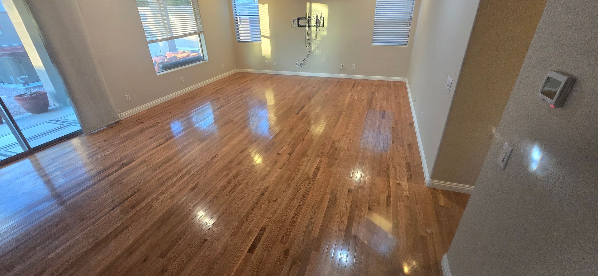 Room with wooden floors, windows, and tan walls. Sunlight reflects off the glossy hardwood.