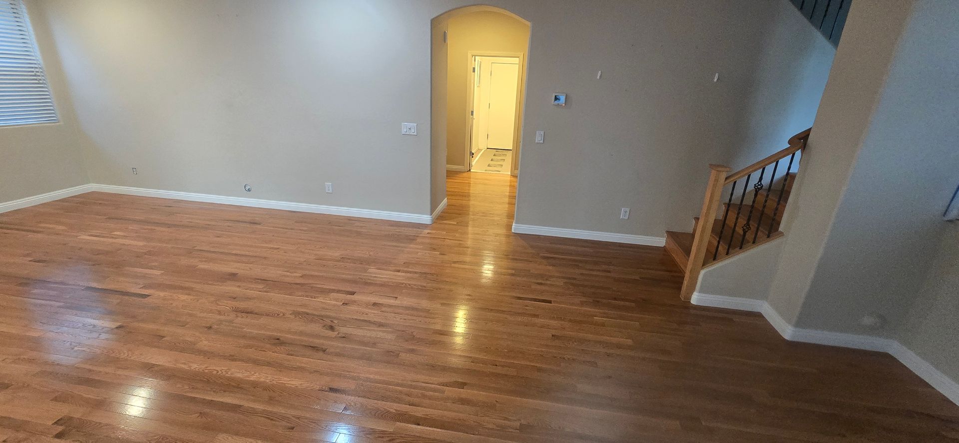 A living room with wooden flooring, a hallway, and a staircase.