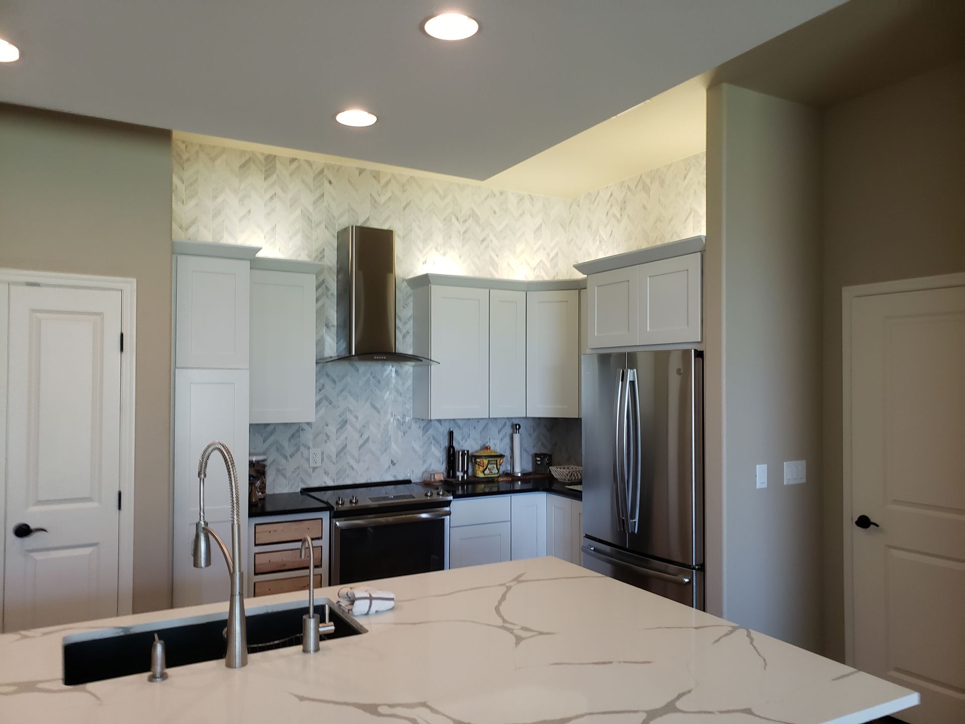 Modern kitchen with white cabinets, stainless steel appliances, and a marble countertop island.