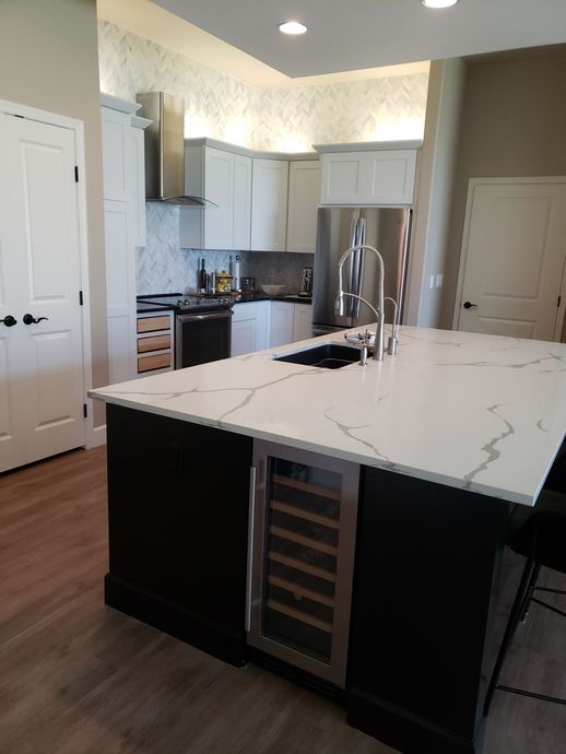 Modern kitchen with white cabinets, dark island, and wine fridge.