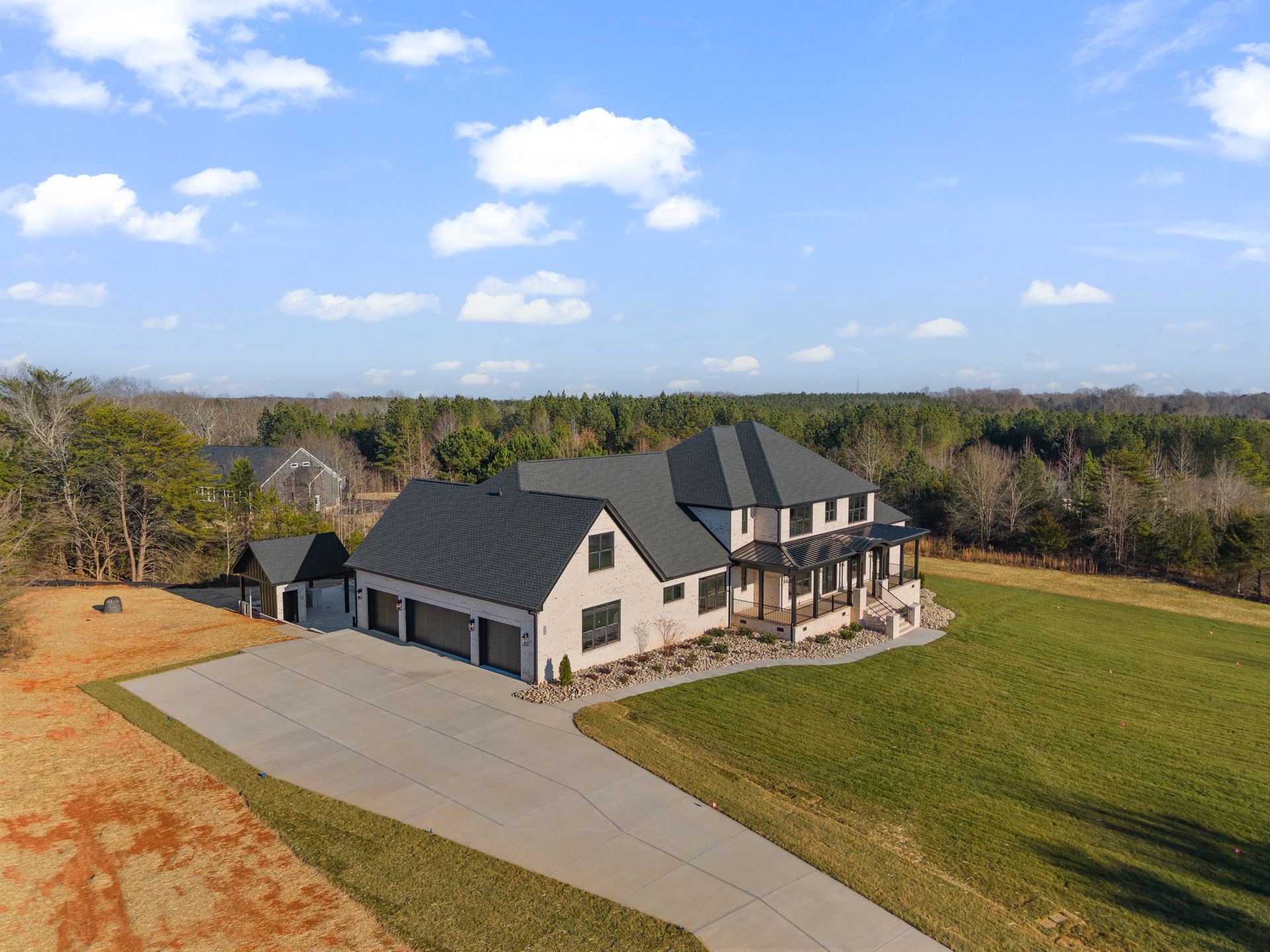 Large beige house with dark roof and driveway on a grassy lot under a blue sky