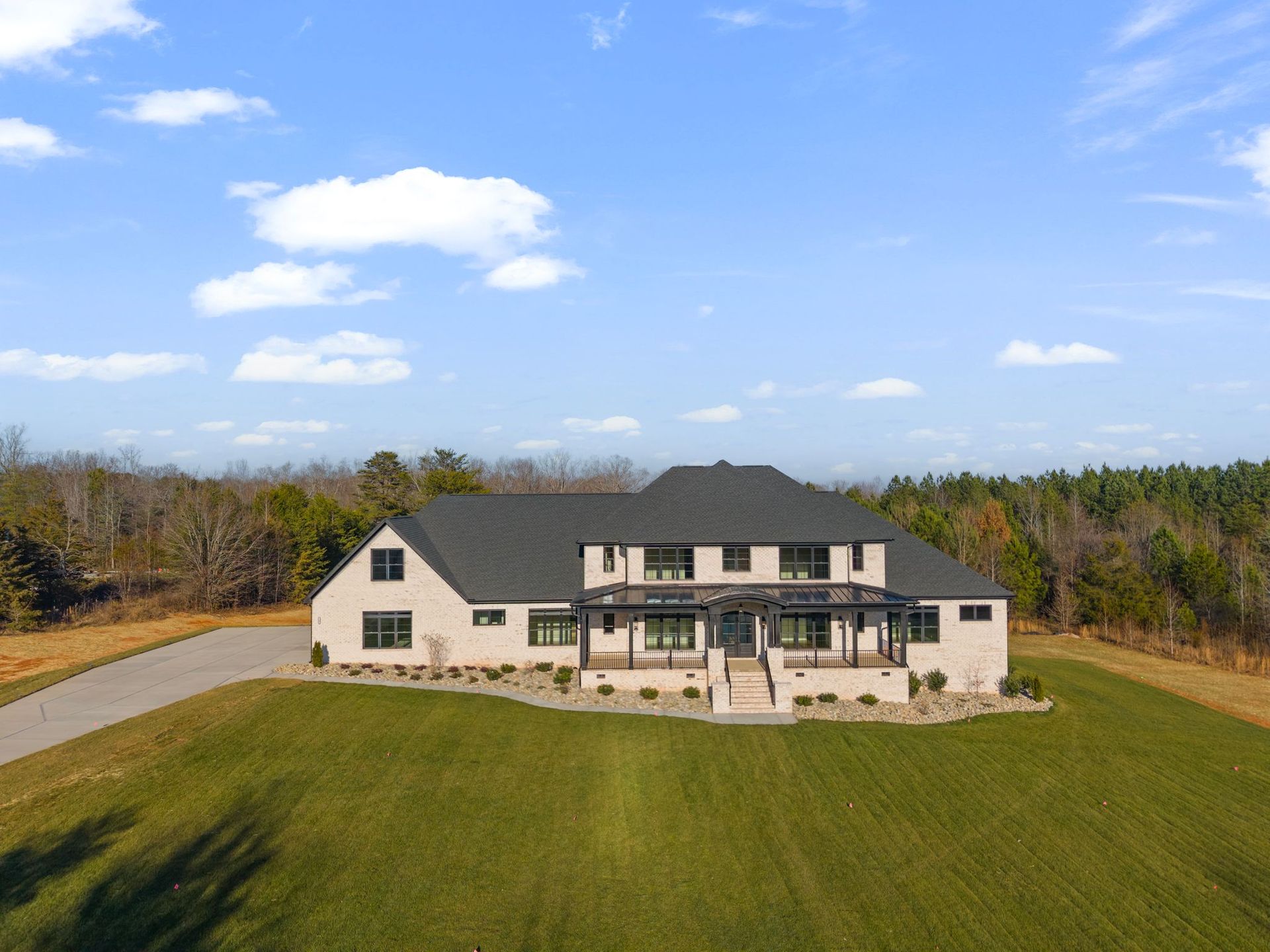 Large cream house with dark roof on a grassy hill under a blue sky, viewed from the front.
