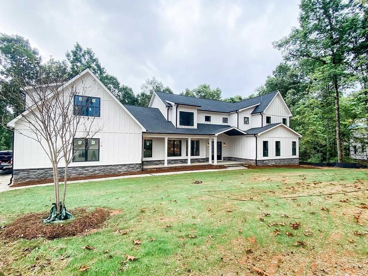 Large white suburban house with a front porch, gray roof, and a grassy lawn surrounded by trees