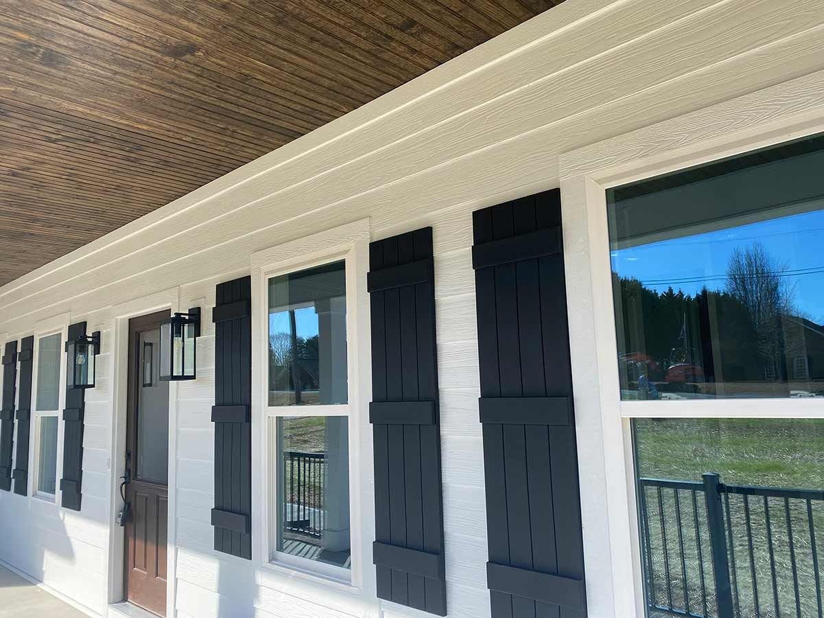 Front porch exterior with white columns, dark shutters, and windows reflecting trees and sky