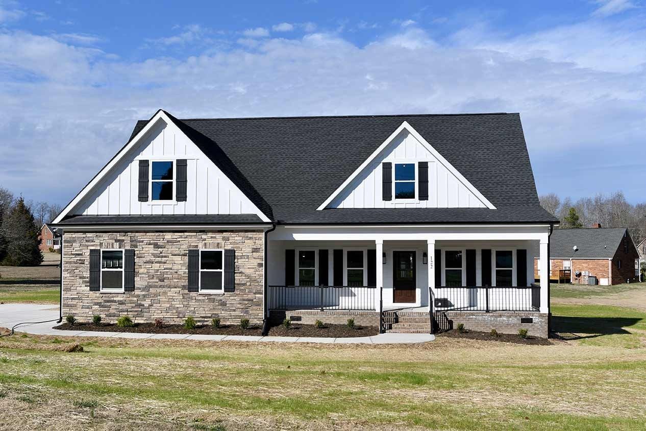 Stone house with white gables and a front porch in a grassy yard under a blue sky